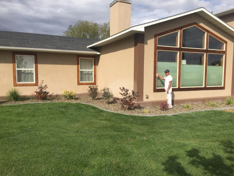 A man is standing in front of a house painting a window.