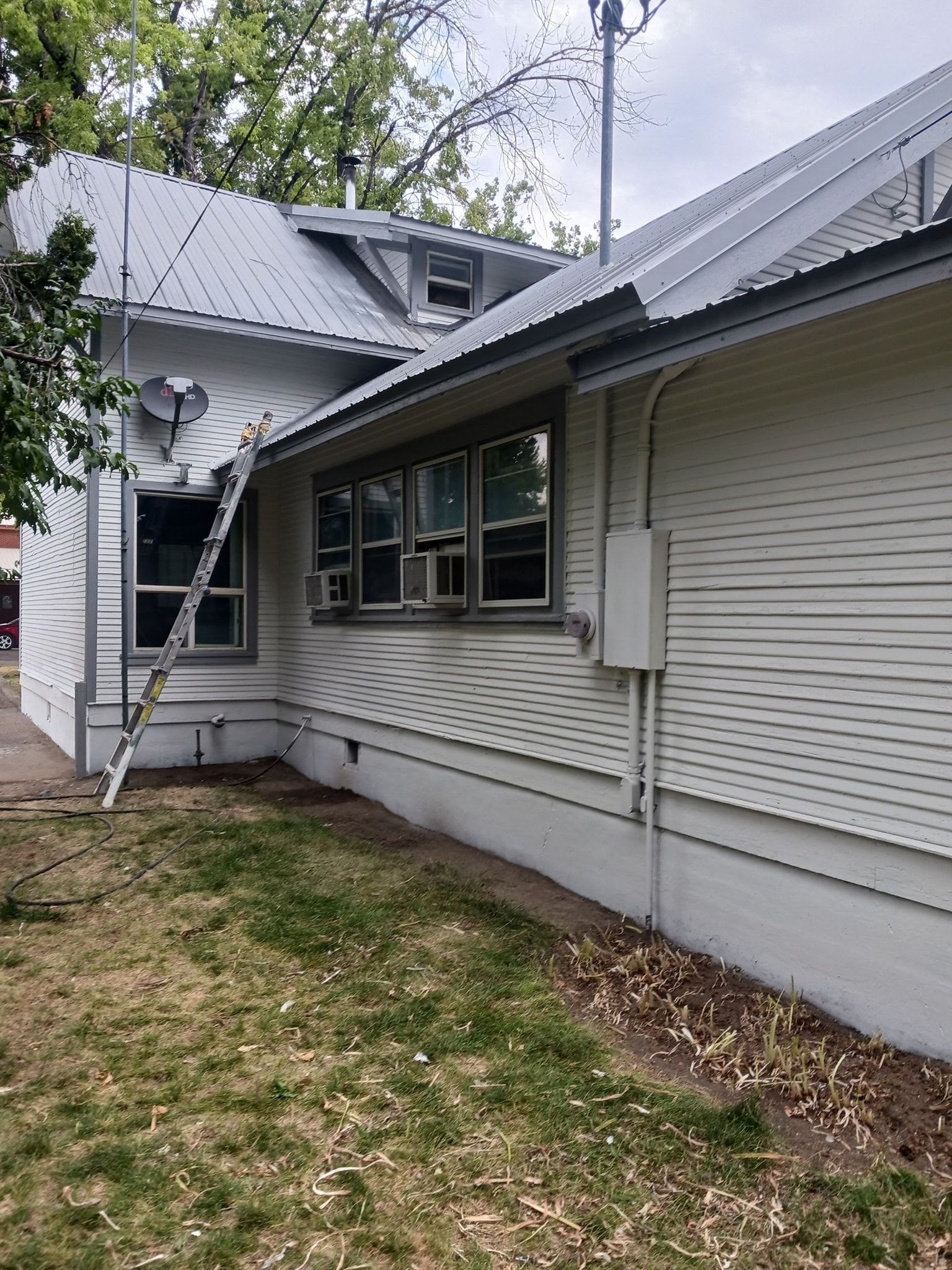A white house with a metal roof and a ladder on the side of it.