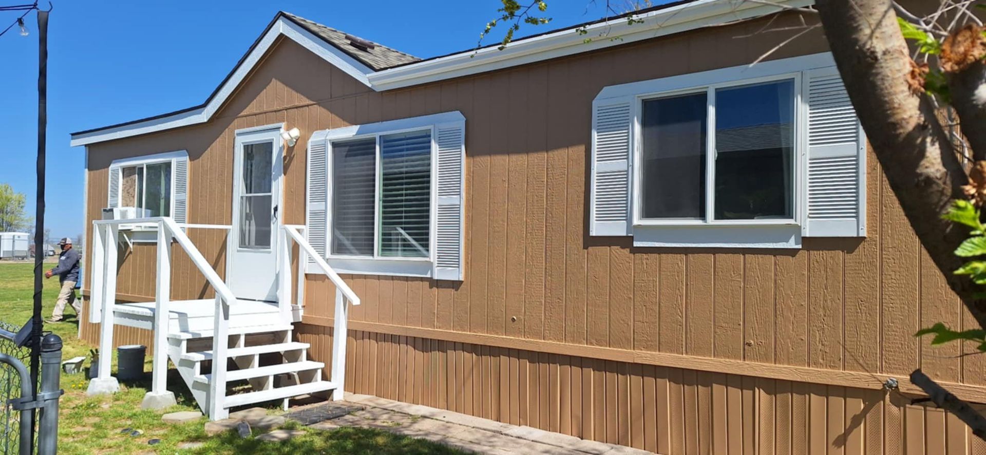 A mobile home with white shutters on the windows and stairs.