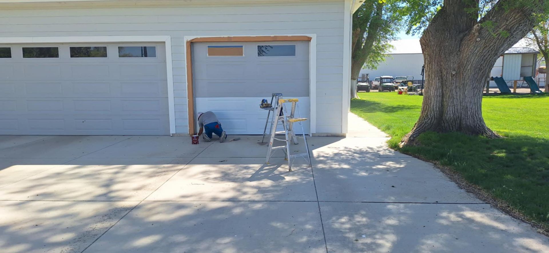 A garage door is being installed in a driveway next to a tree.