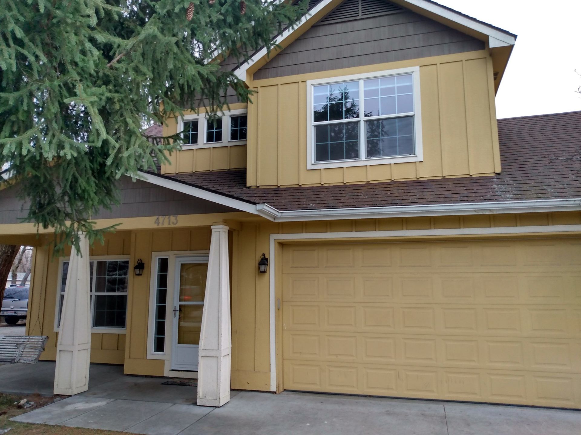 A yellow house with a garage and a tree in front of it