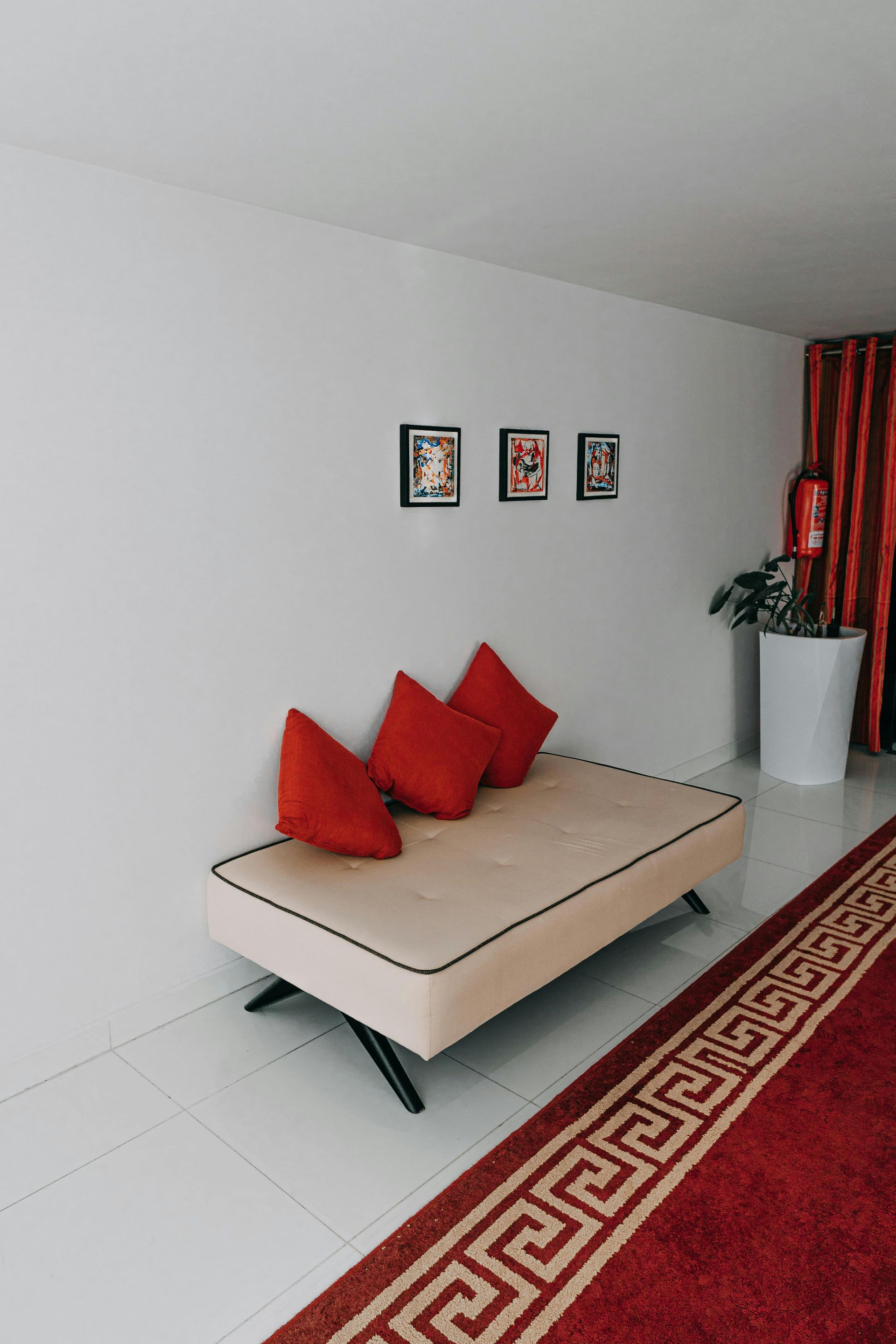 A couch with red pillows is sitting in a room next to a red rug.