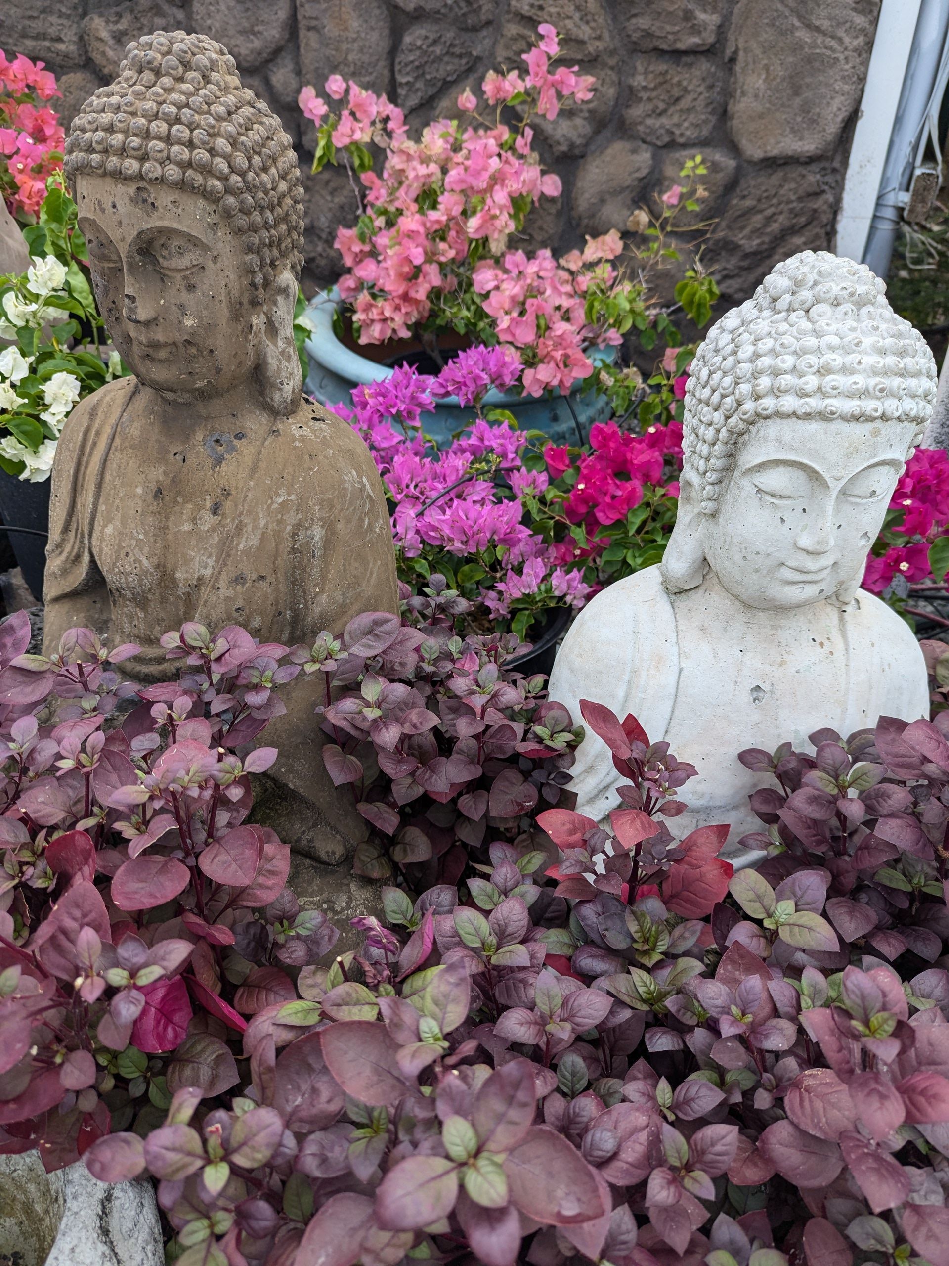 Two statues of buddhas are sitting in a garden surrounded by flowers.
