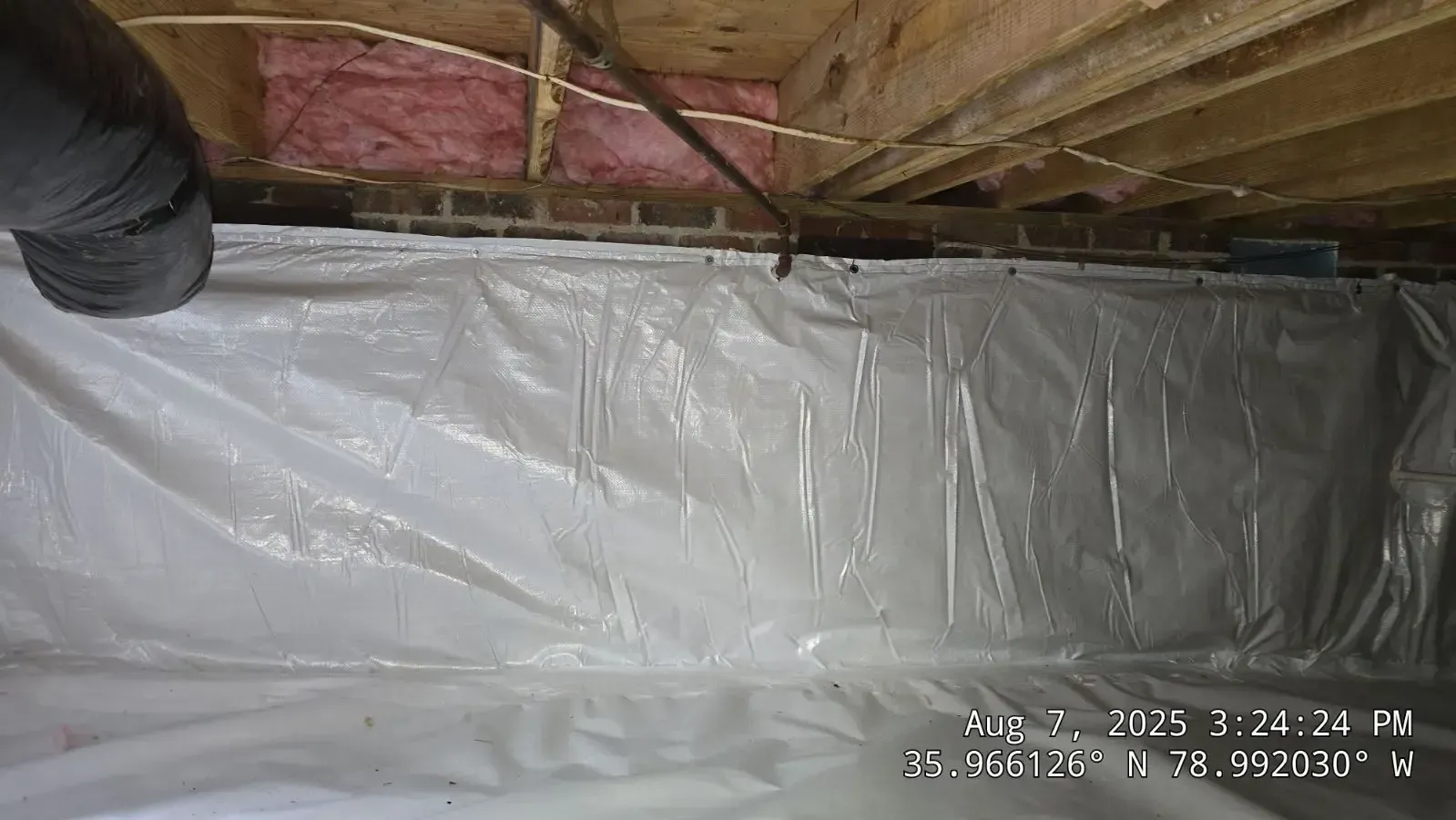 White vapor barrier in a crawl space under a wooden structure.