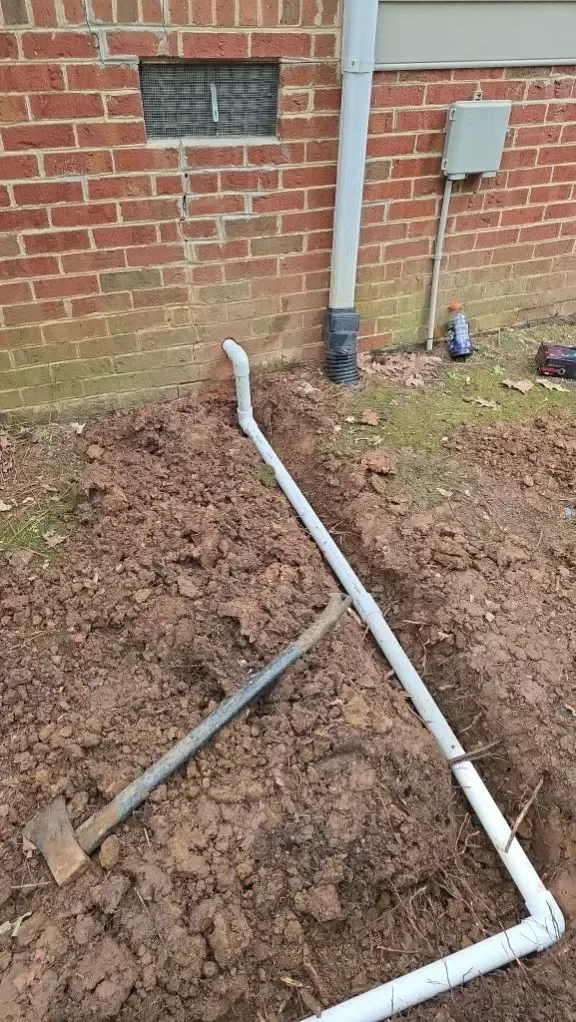 Construction site with exposed white pipes, brick wall, and tools in dirt.