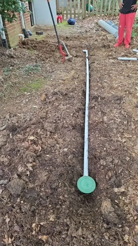 A buried septic system pipe and access point in a residential backyard; person in pink pants nearby.