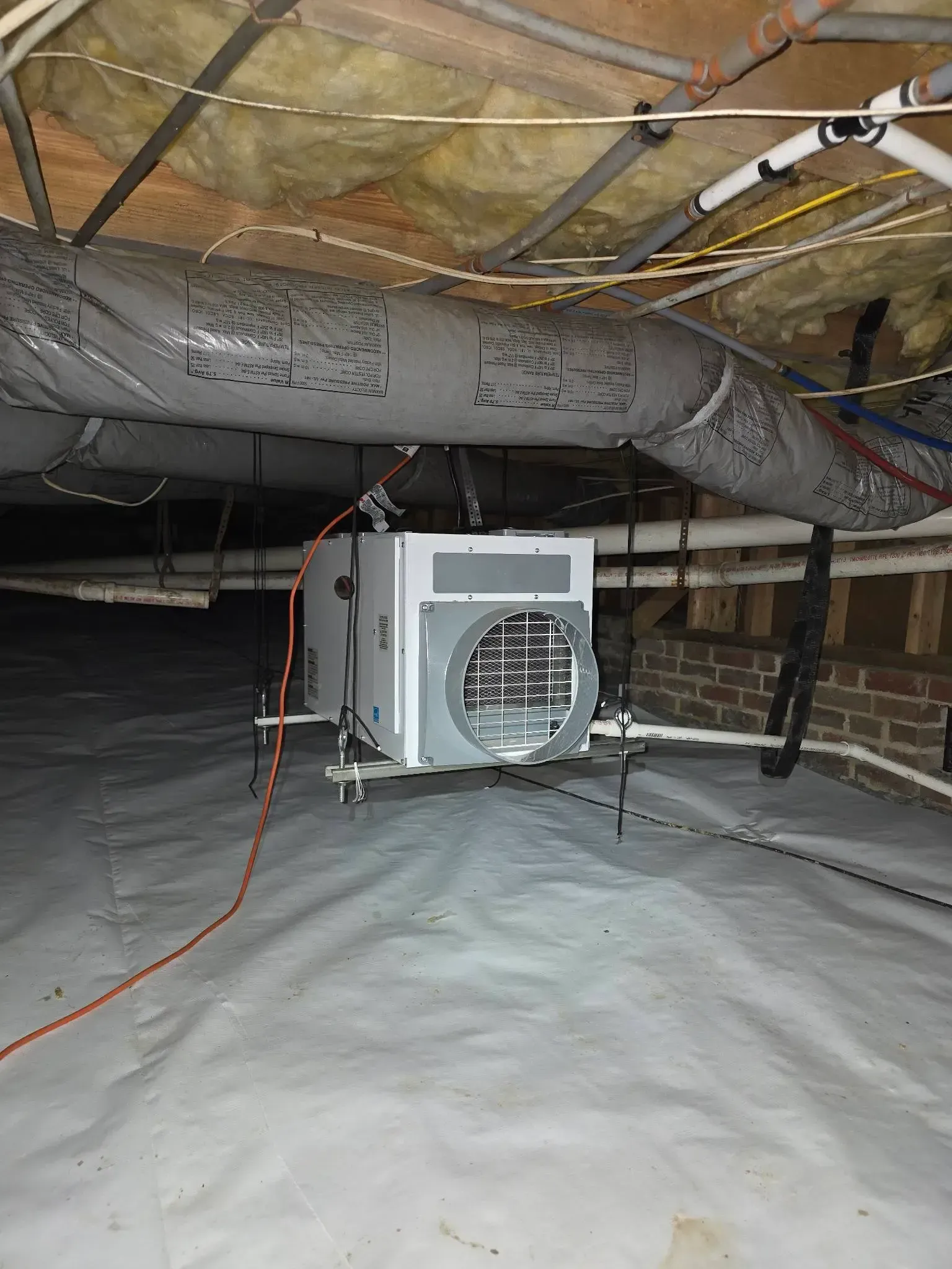White crawl space with a dehumidifier suspended from the ceiling, ductwork and piping present.