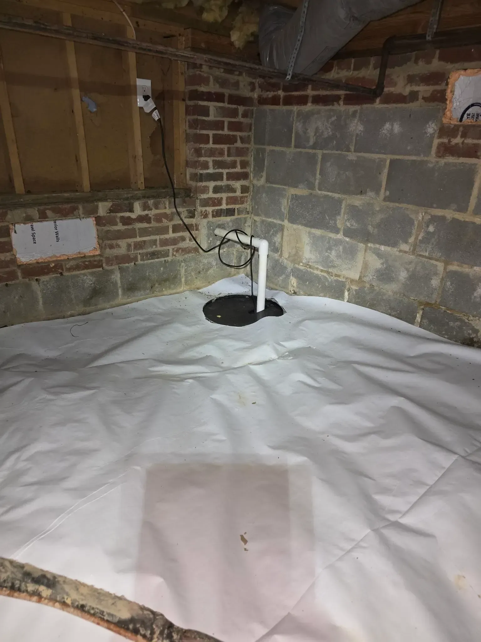 Basement with white vapor barrier flooring, sump pump, brick and concrete block walls.