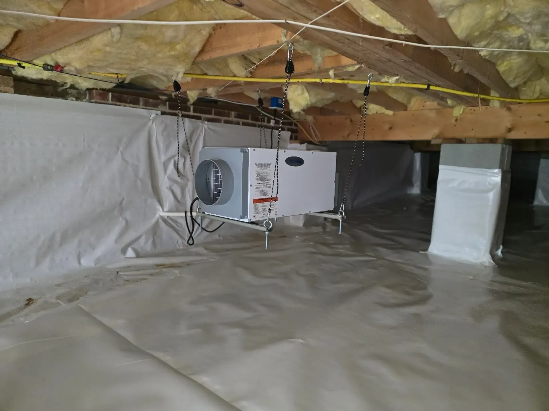 Crawl space with white vapor barrier, wooden beams, HVAC unit.