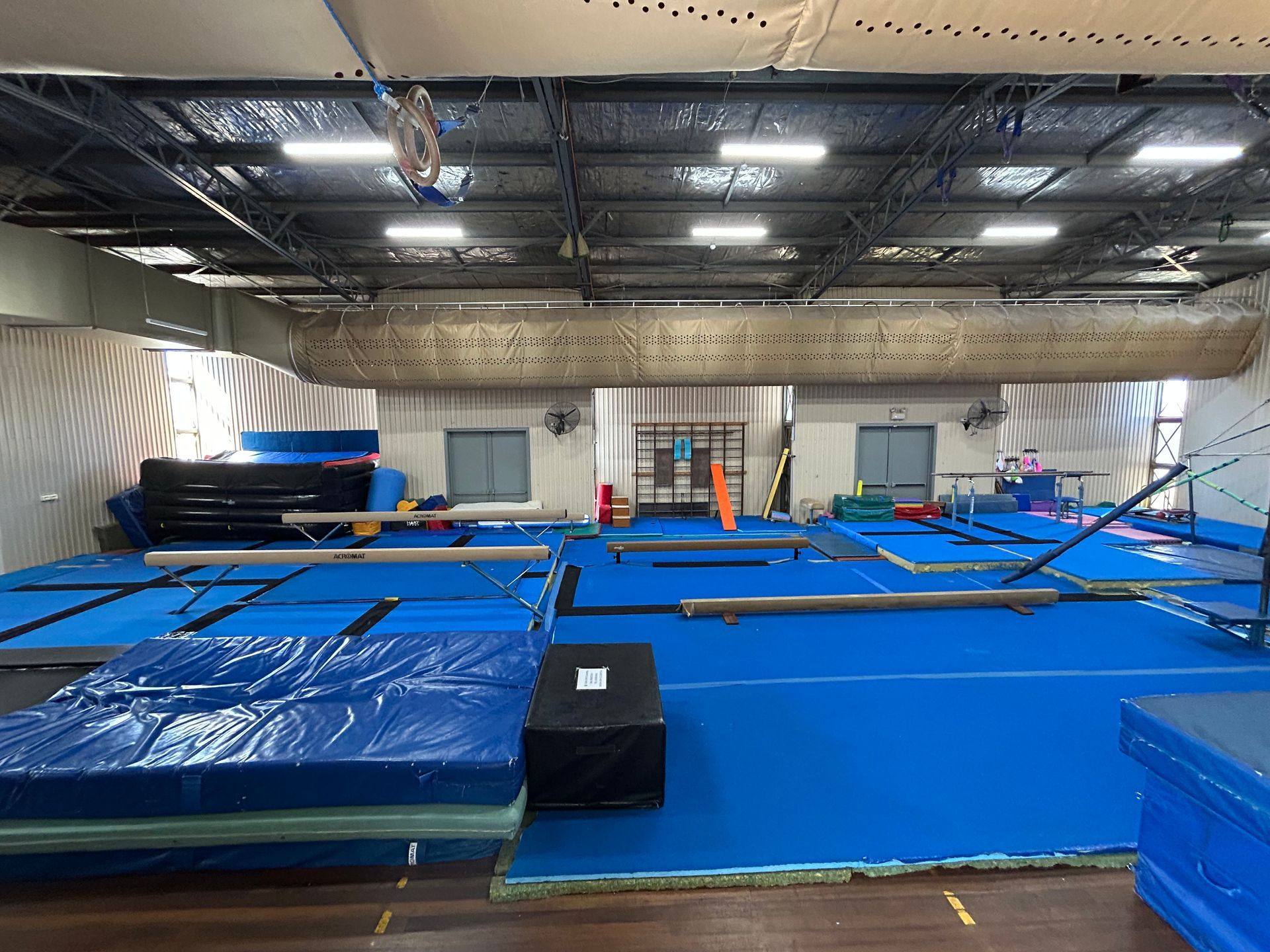 Gymnasium interior with blue mats, balance beams, and gymnastics equipment.