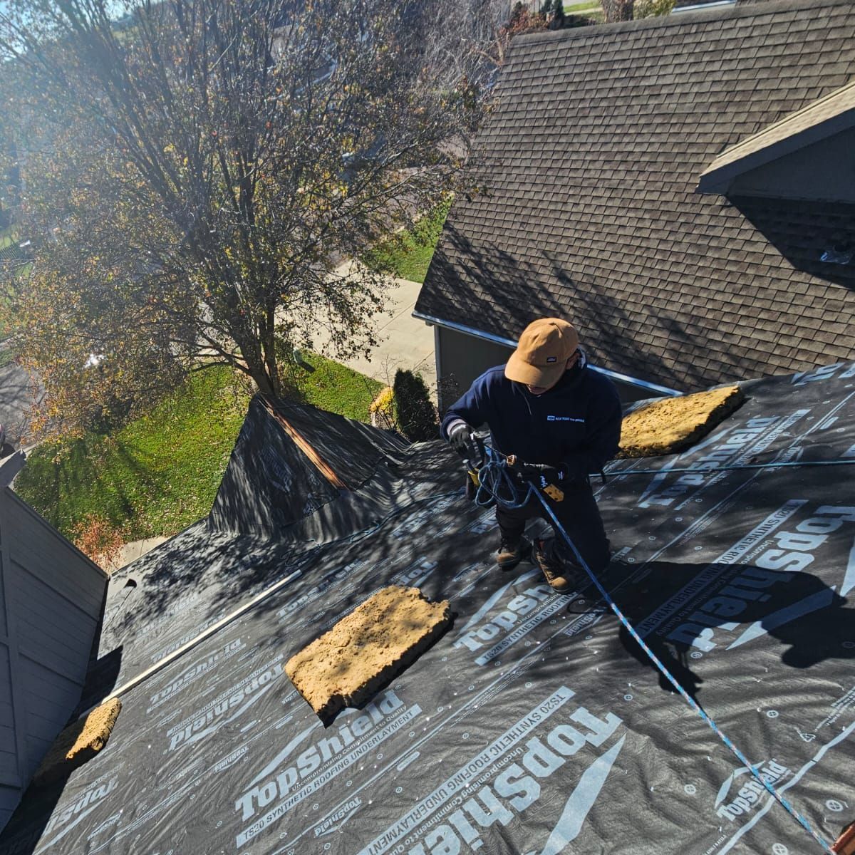 A man is working on the roof of a house with topshield shingles