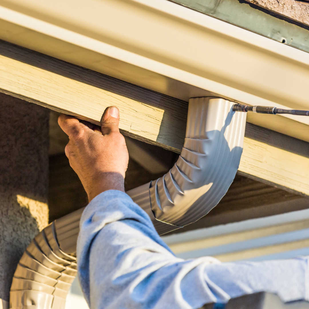 A man is fixing a gutter on the side of a house.