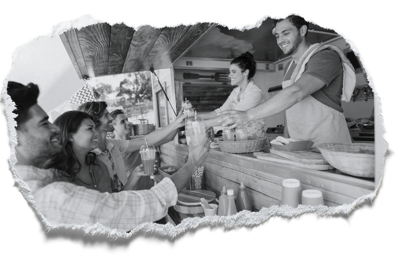 People ordering food at a food truck, smiling. Server hands food over counter to customer. Outdoors, day.