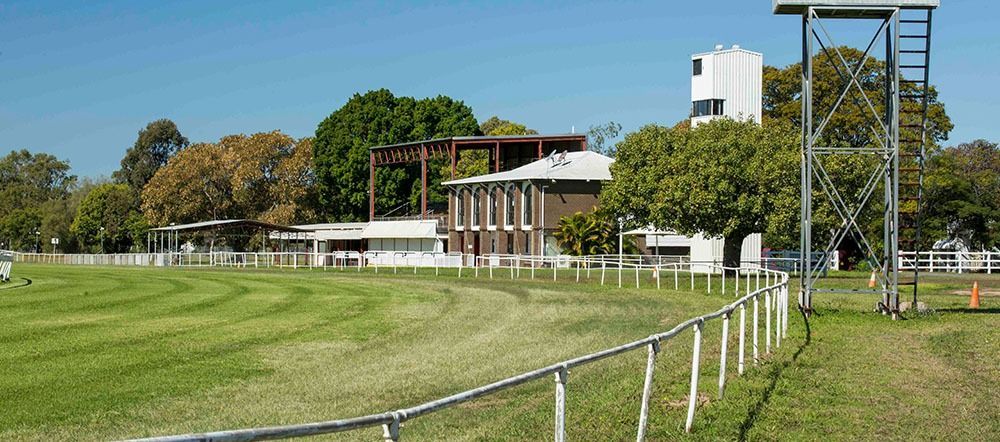 A Large Grassy Field With A Fence And A Building In The Background — Angels for Pets In Emerald, QLD