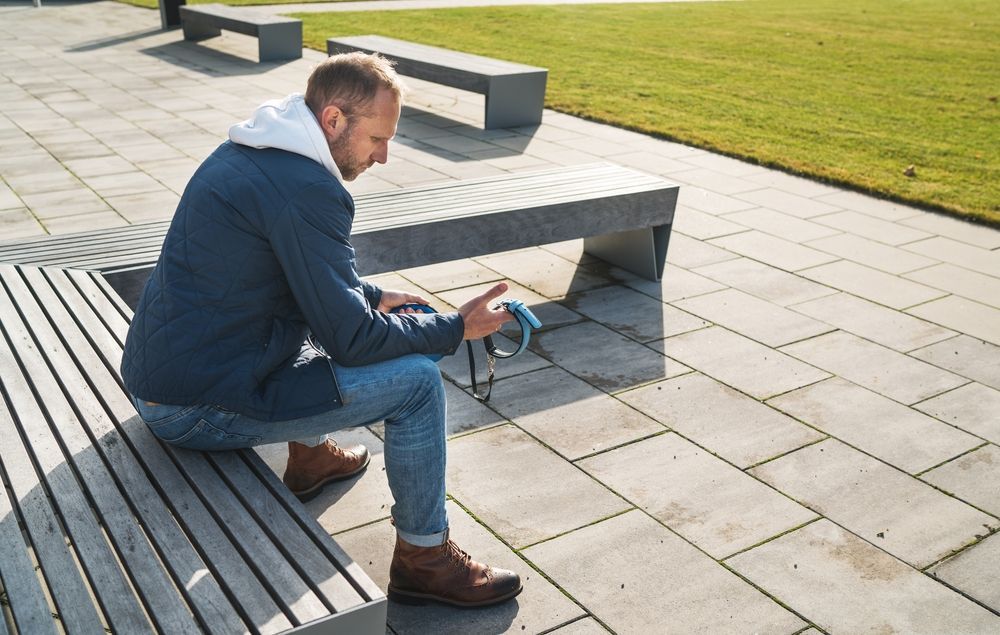 A Man Is Sitting On A Bench Looking At His Dog Collar — Angels for Pets In Tanby, QLD