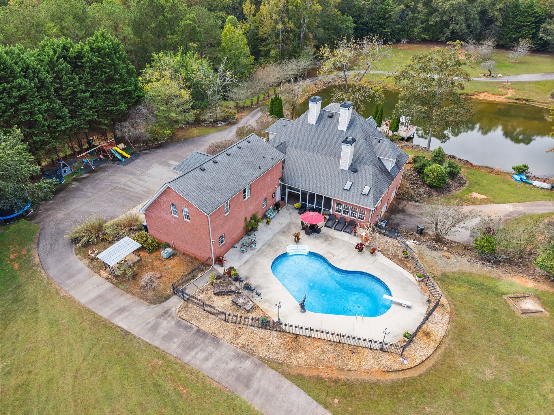 Gainesville Georgia Home - Aerial view of a brick house with a pool, pond, and driveway surrounded by green trees and grass.