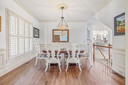 A kitchen with white cabinets , wooden floors , stainless steel appliances and a large island with chairs.