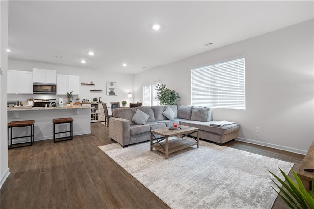 Open-concept living space with a gray sectional sofa, kitchen, and wood flooring.