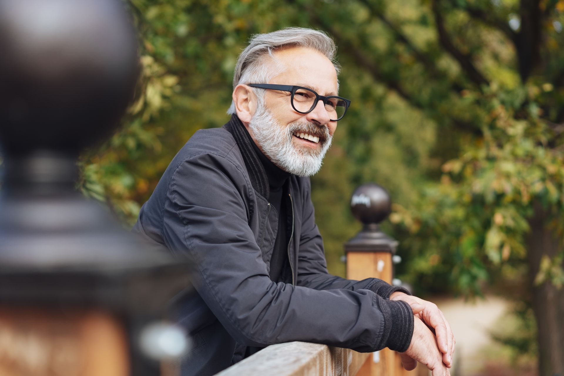 A man with a beard and glasses is leaning on a wooden railing.
