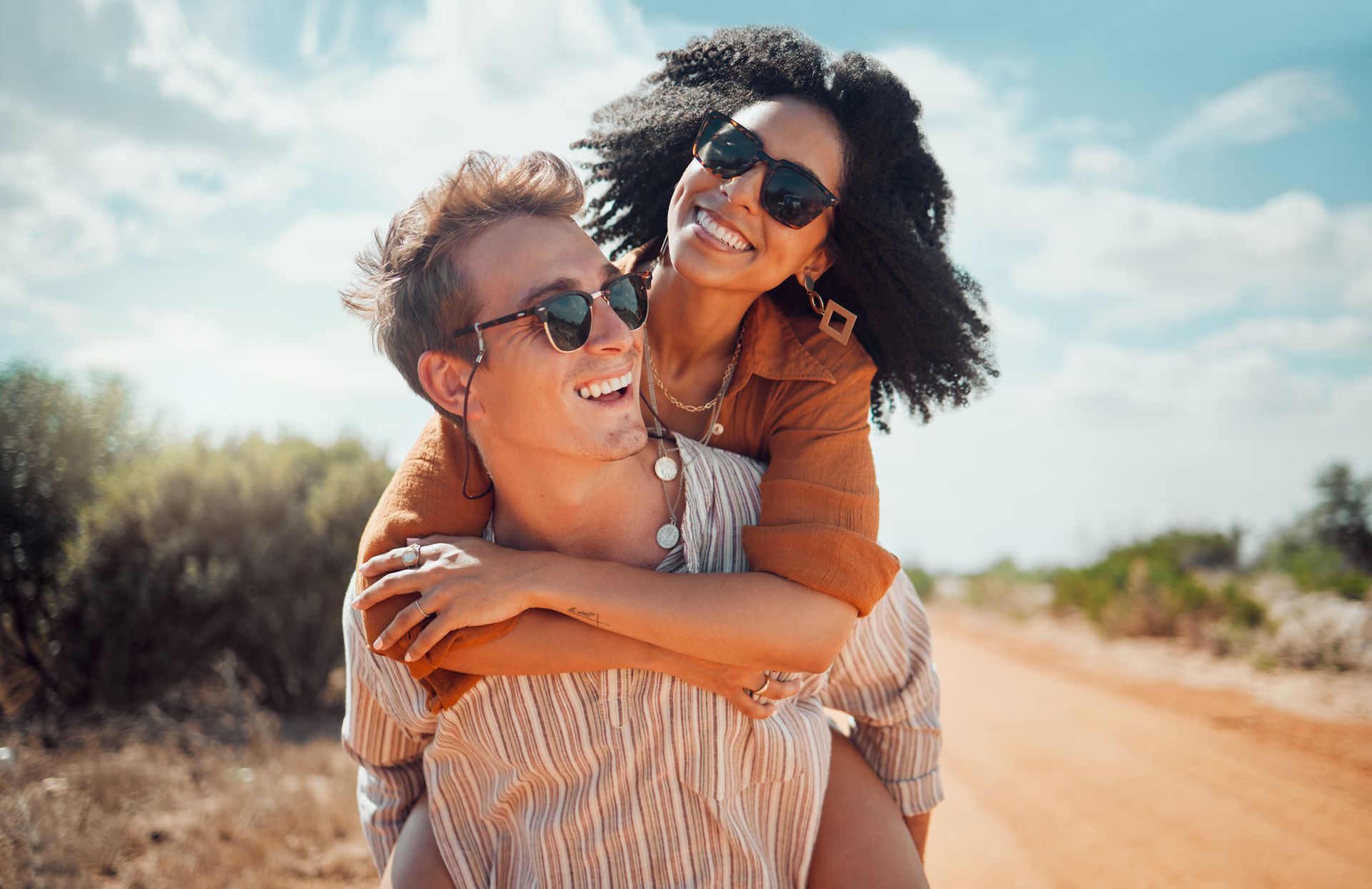 Two women are laughing and hugging each other on a dirt road.