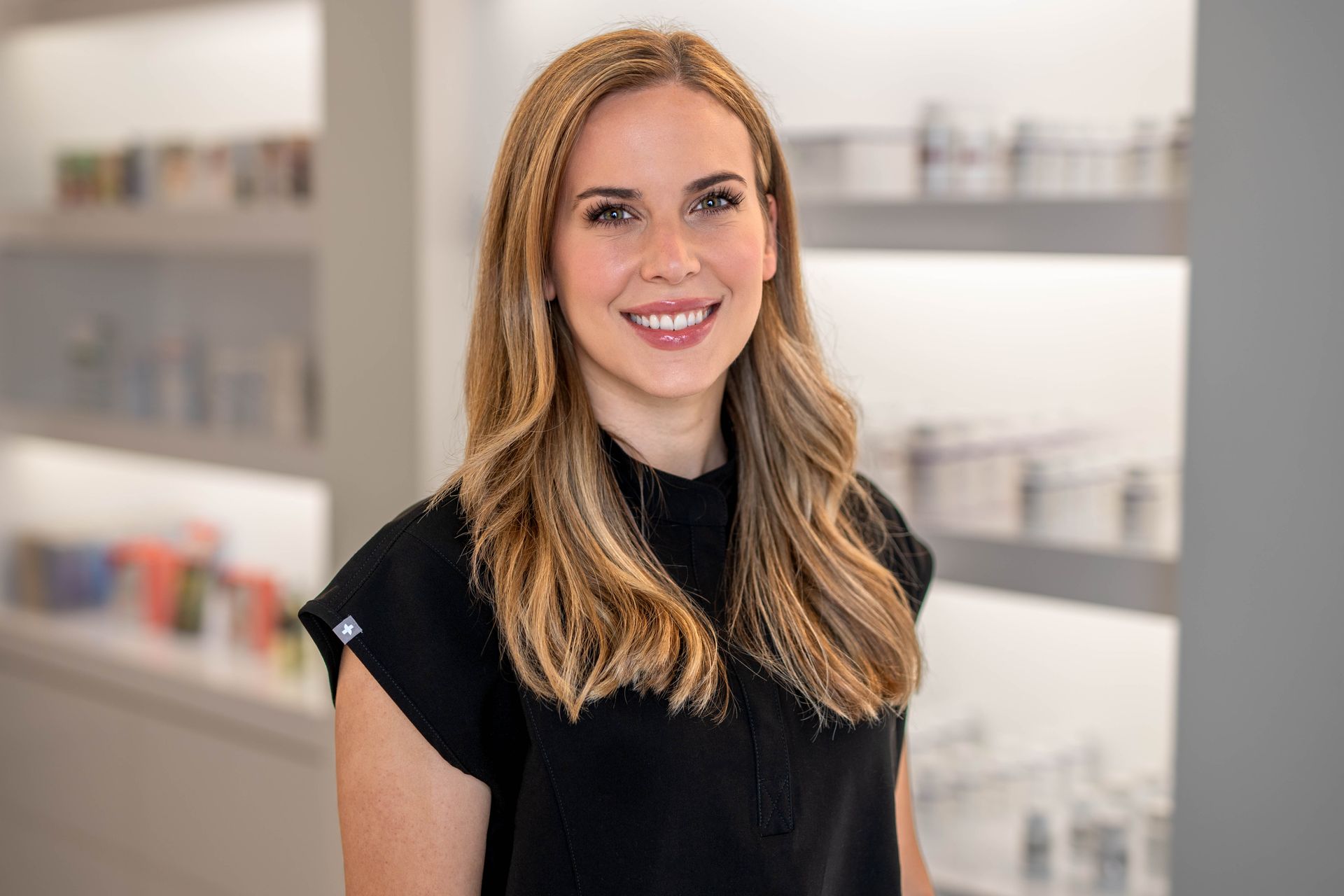 A woman in a black shirt is standing in front of a shelf of cosmetics.