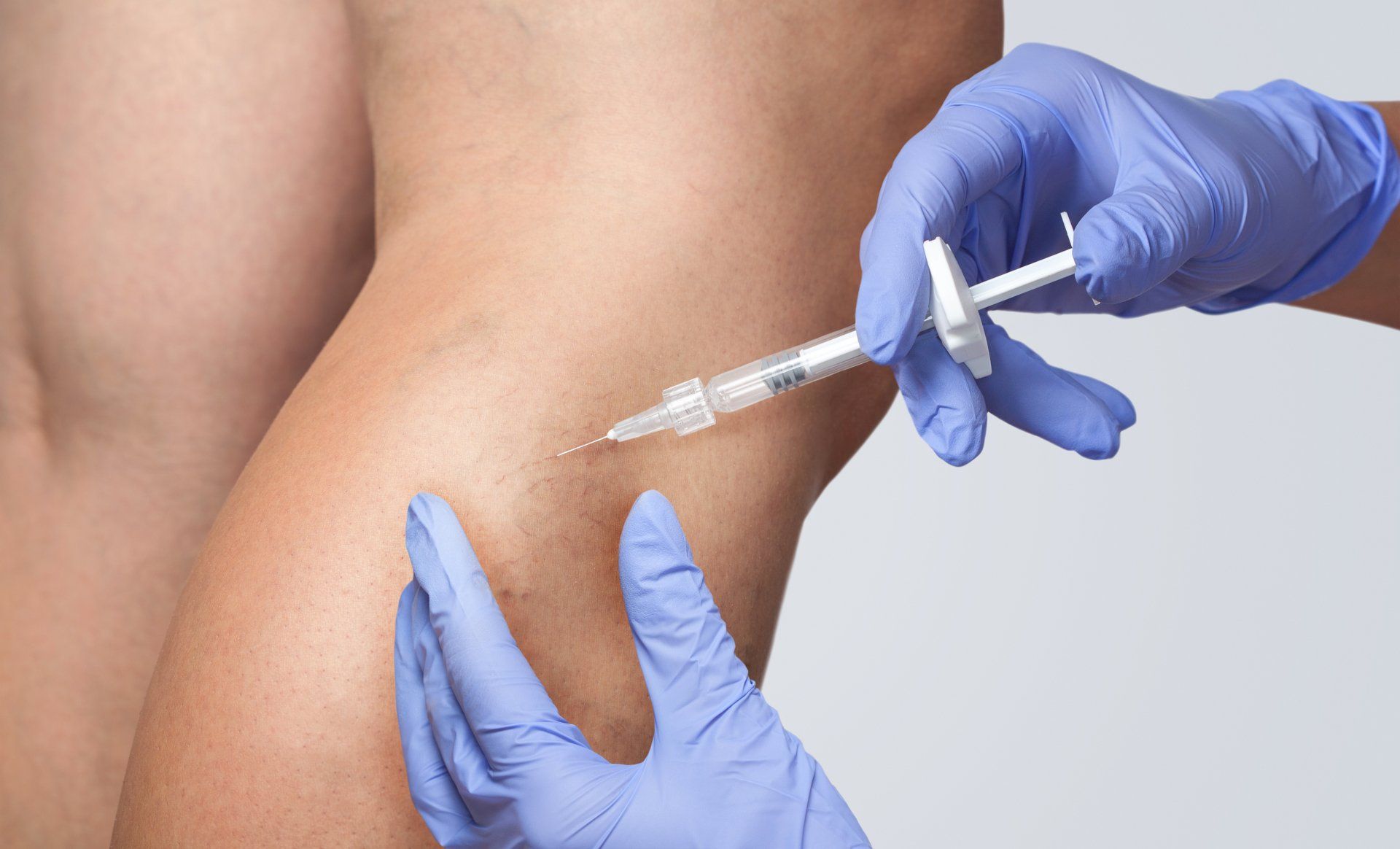 A person is getting an injection in their leg with a syringe.
