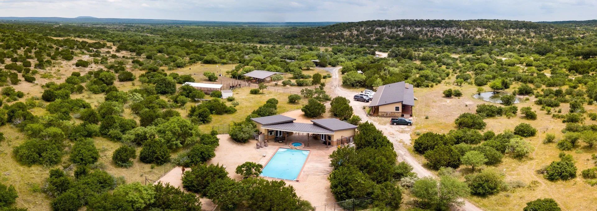 Aerial view of a home with a pool in a rural, green landscape under a cloudy sky.