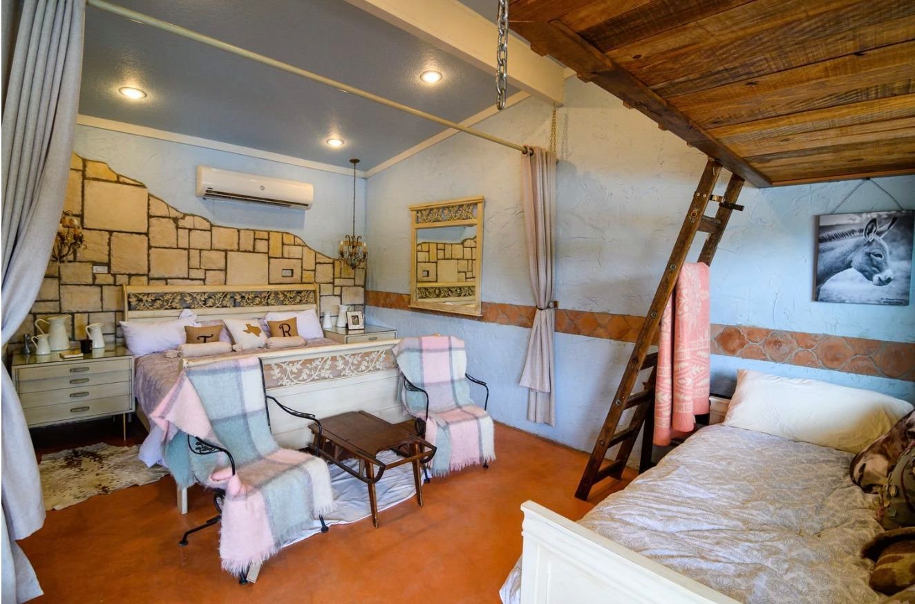 Bedroom with bed, seating, loft bed, stone wall, and light blue walls.