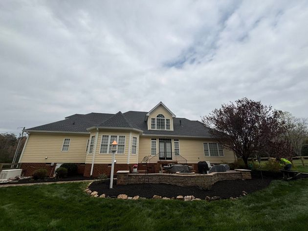 A large house with a gray roof is sitting on top of a lush green field.
