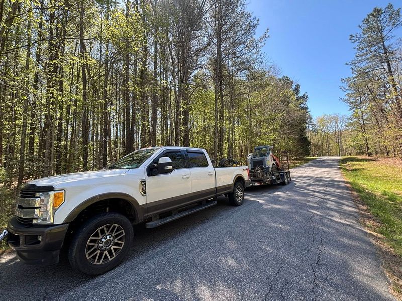 A white truck is parked on the side of a road next to a forest.