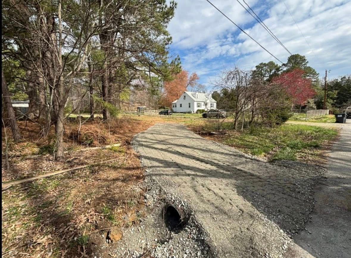 A dirt road going through a forest with a white house in the background.