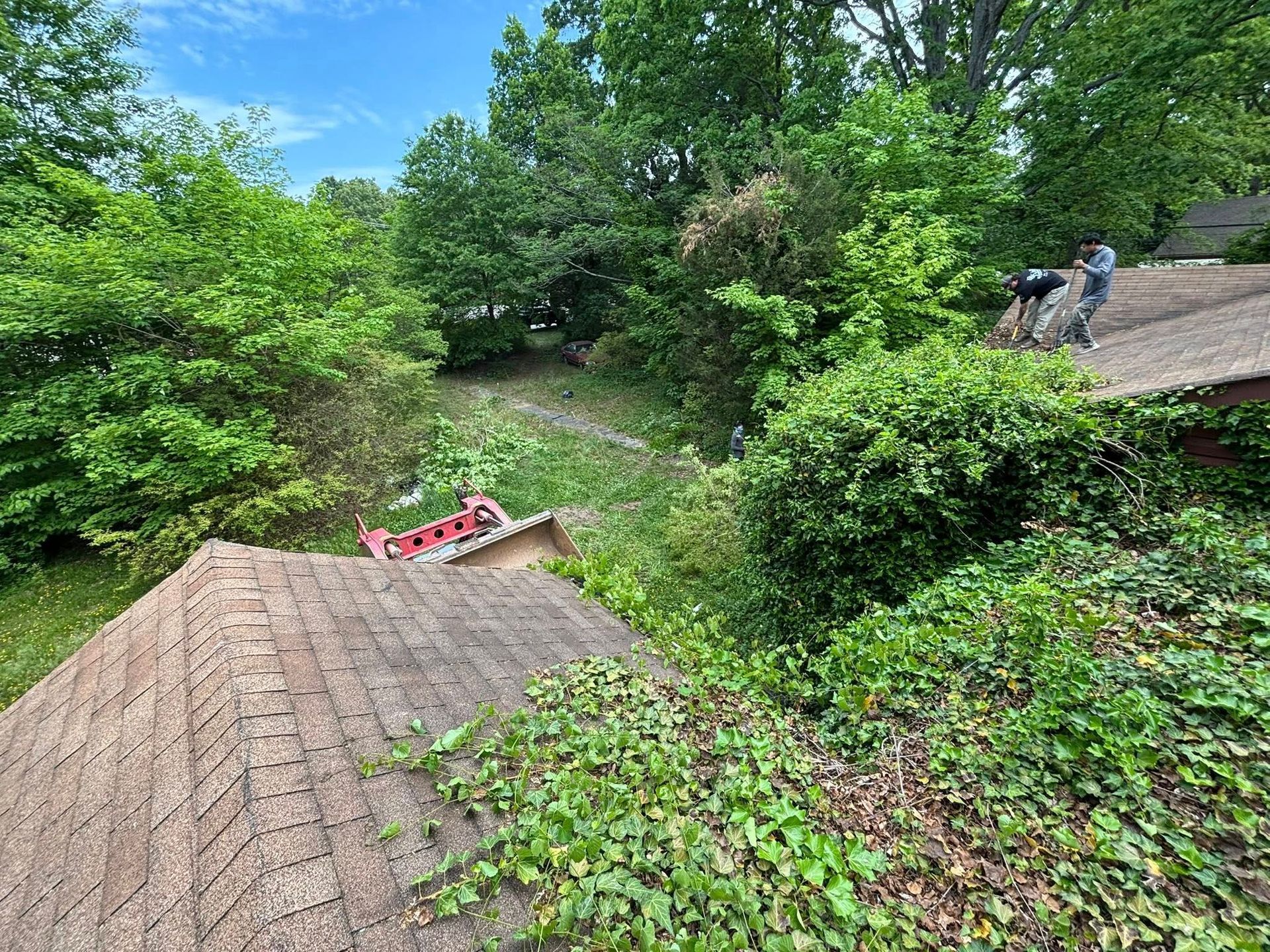 A man is working on the roof of a house surrounded by trees.