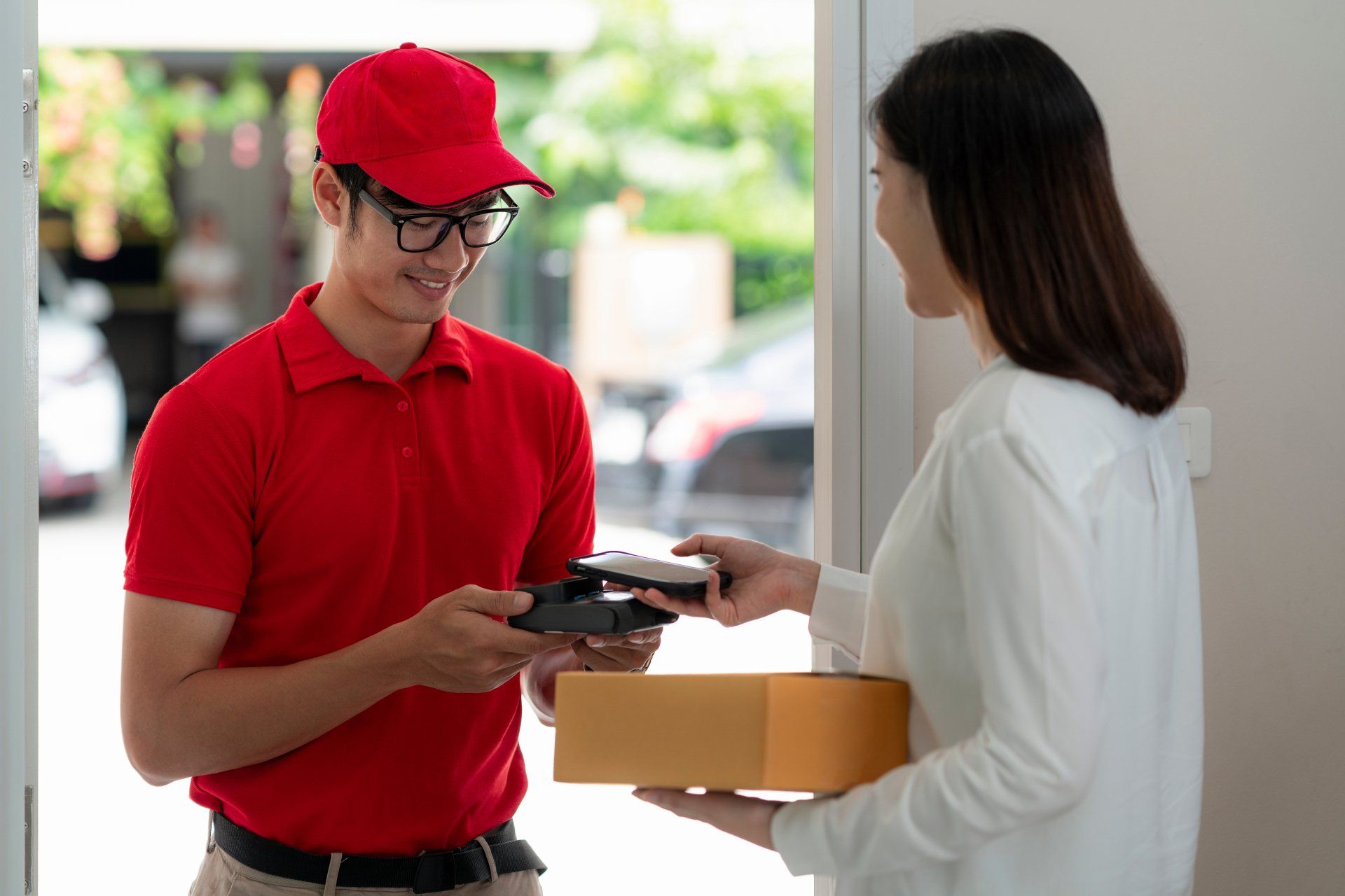 home delivery service man in red uniform and young woman customer appending signature in digital mobile phone receiving parcel