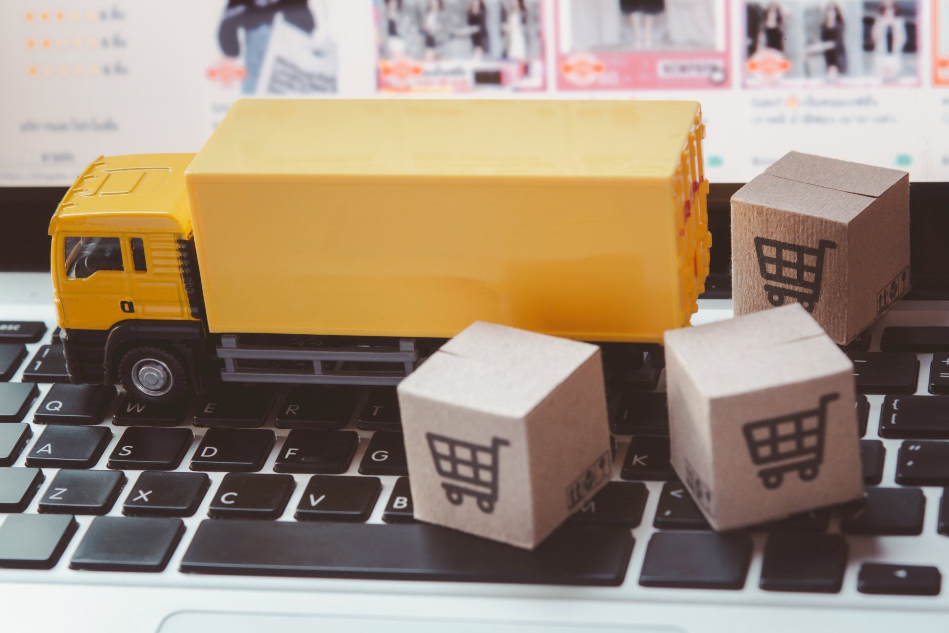 Truck and paper cartons or parcel with a shopping cart logo on a laptop keyboard