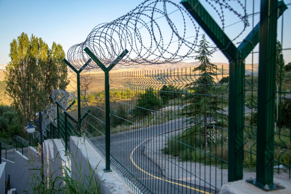Green Fence Topped With Razor Wire; Road Winds Through Hilly Landscape — Keith Dellit Rural Fencing in Yandina Creek, QLD