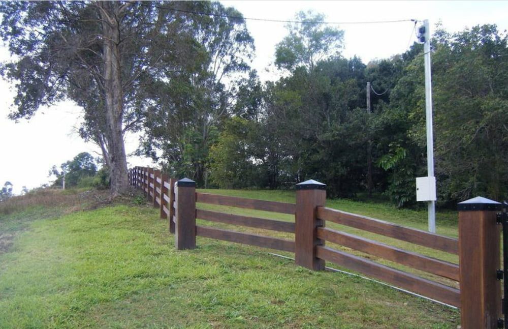 Wooden Fence on a Grassy Hill With a Large Tree, Surrounded by Greenery — Keith Dellit Rural Fencing in Yandina Creek, QLD