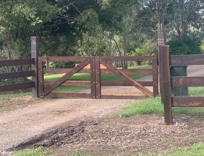Wooden Gate With Diagonal Bracing, on a Dirt Driveway, in Front of Trees — Keith Dellit Rural Fencing in Yandina Creek, QLD