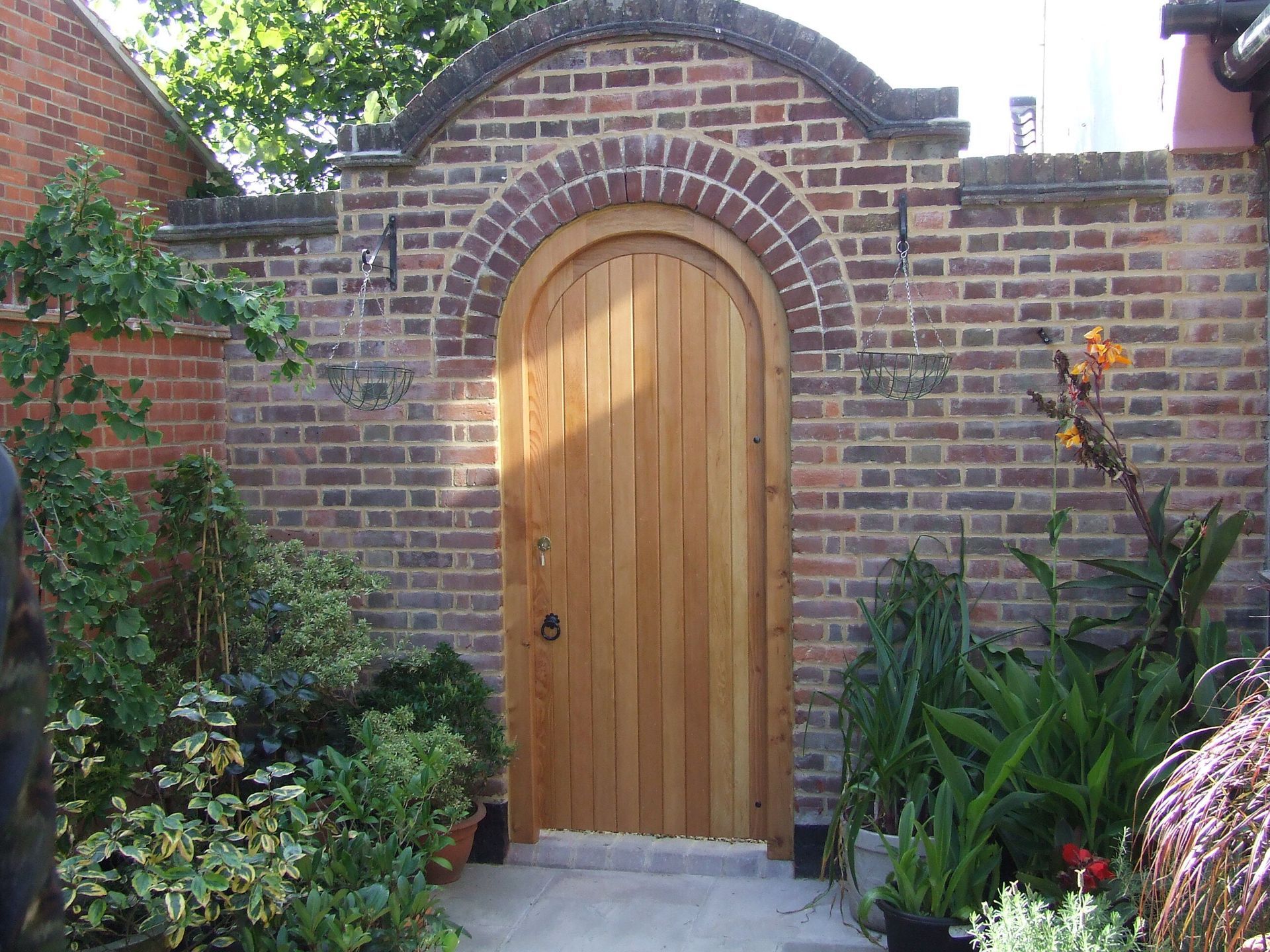 A brick wall with a green gate leading to a garden
