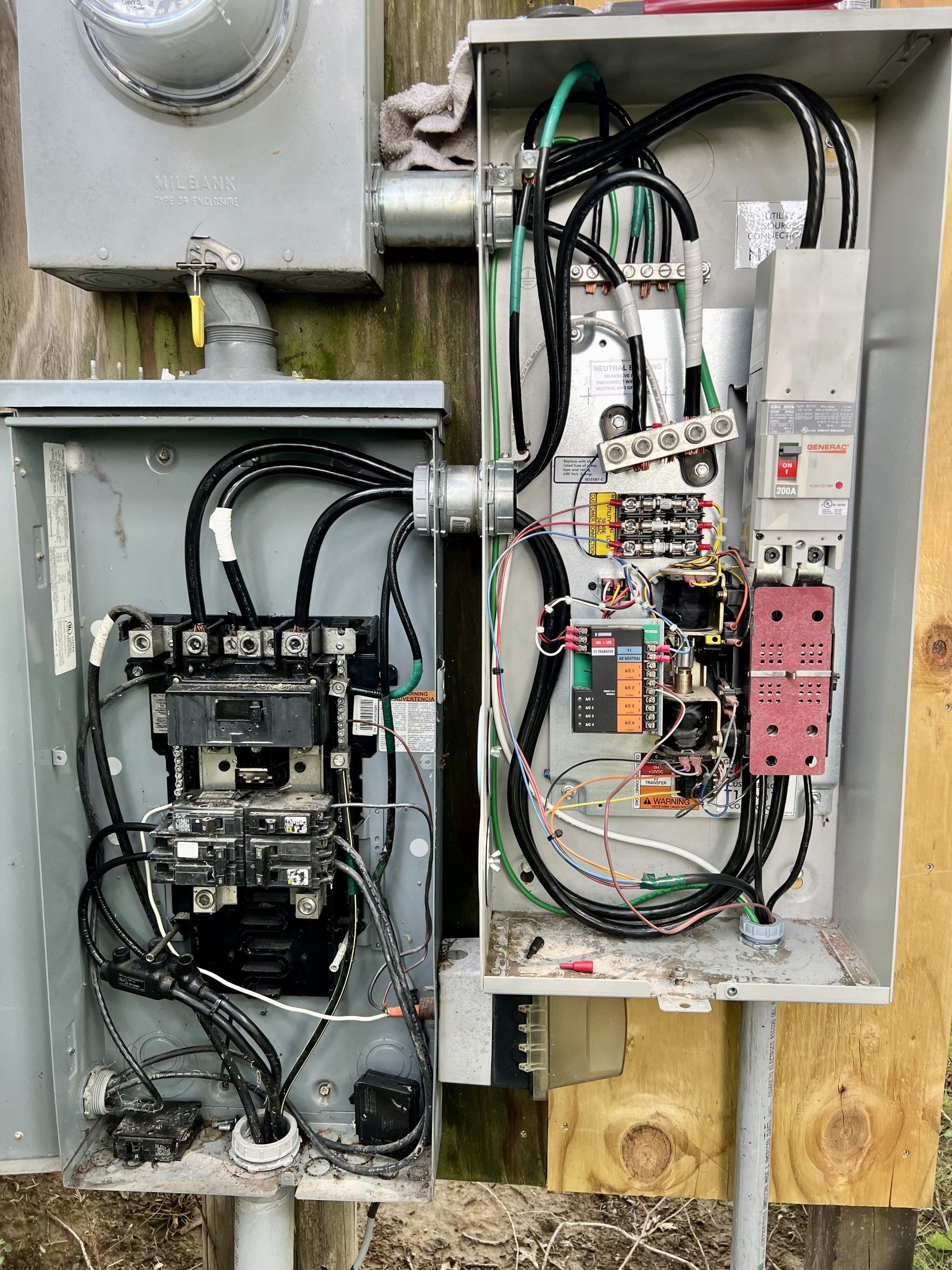 Two gray electrical boxes mounted on wood; one meter box, wires visible.