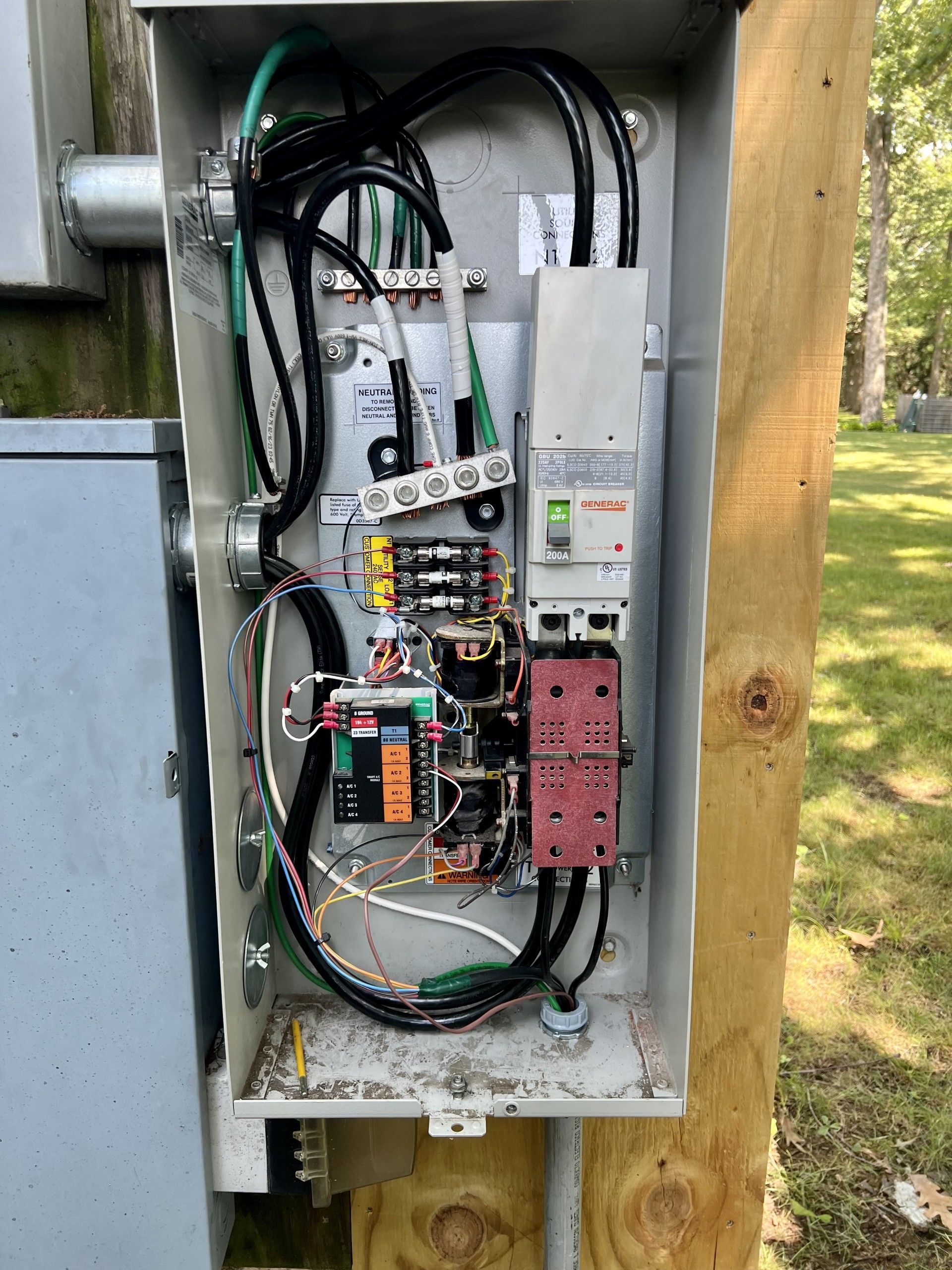 Open electrical panel on a wooden post; contains wires, circuit breakers, and other electrical components.