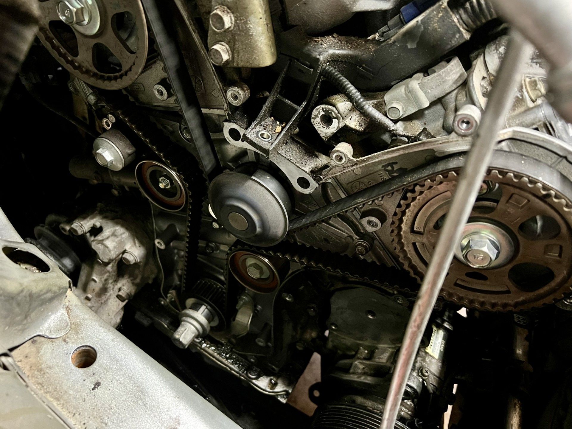 Close-up of a car engine with belts and pulleys, oily, likely for repair.