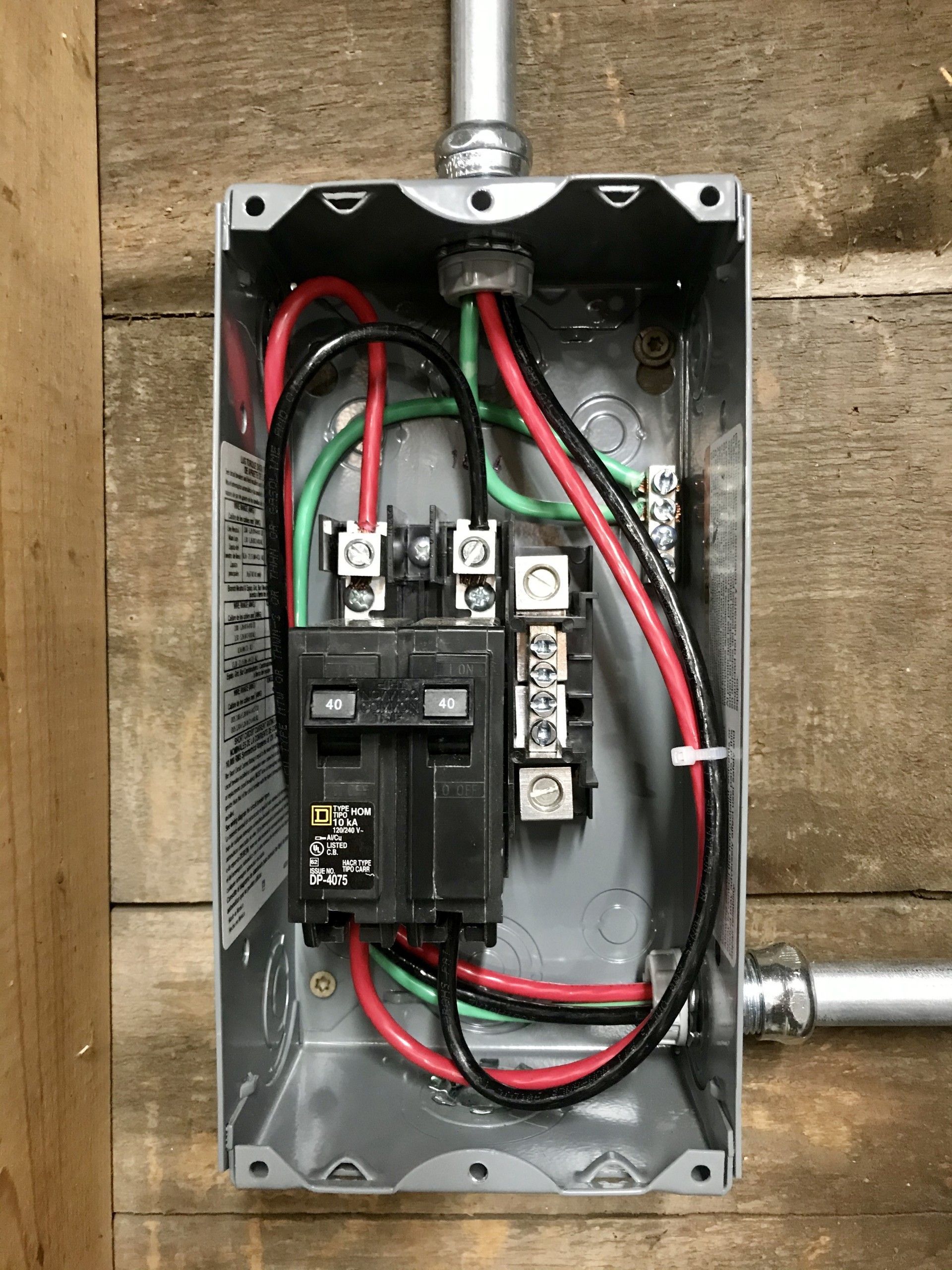 Electrical junction box with circuit breakers, wires, and conduit. Black, red, and green wires visible.