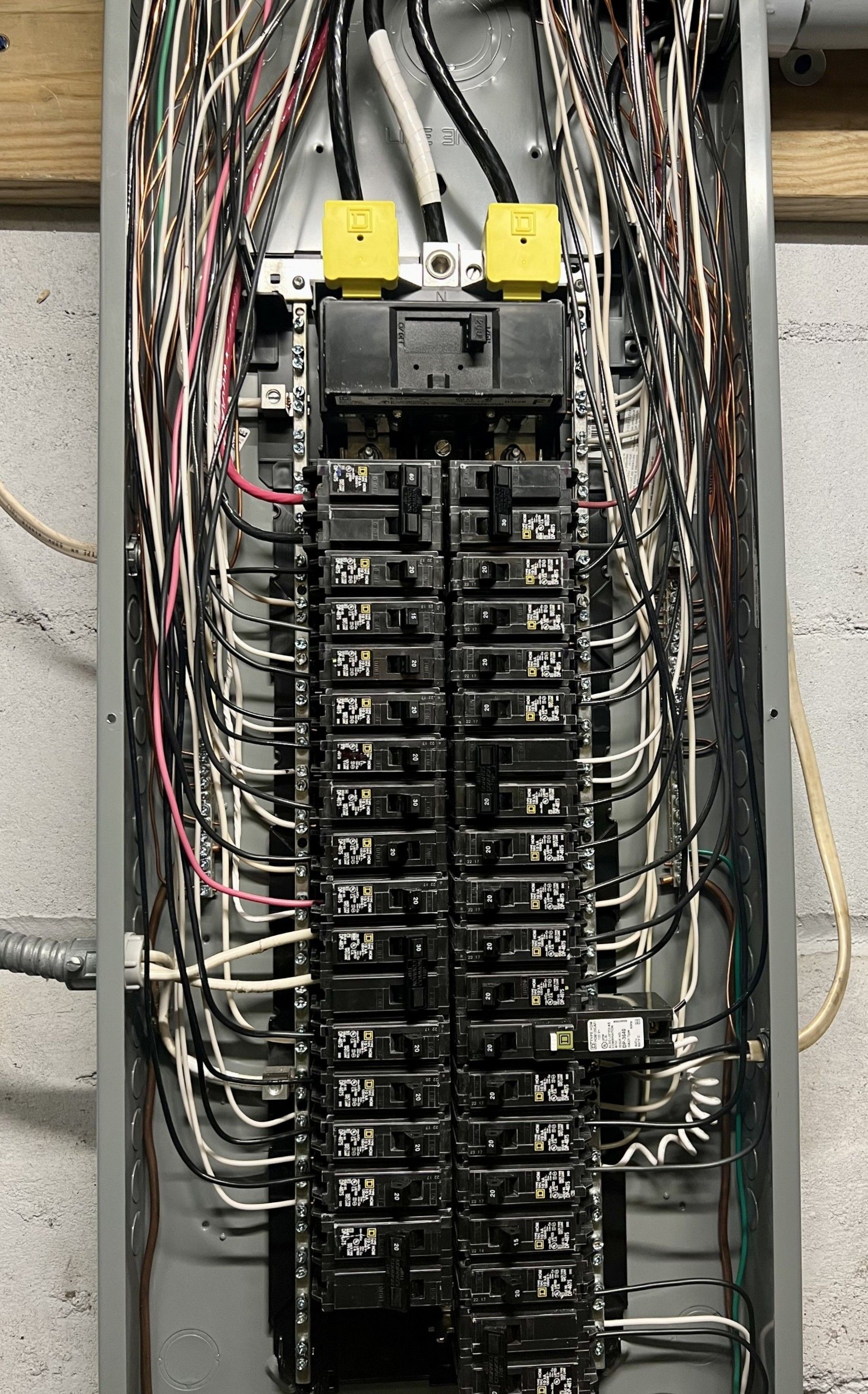 Electrical panel with many wires and breakers. Silver panel mounted on a gray wall.
