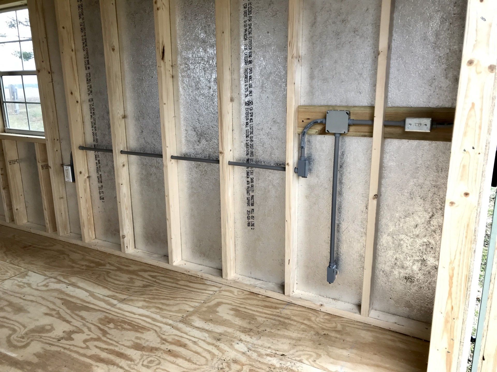 Interior of a building under construction, showing wooden frame, insulation, and electrical wiring.