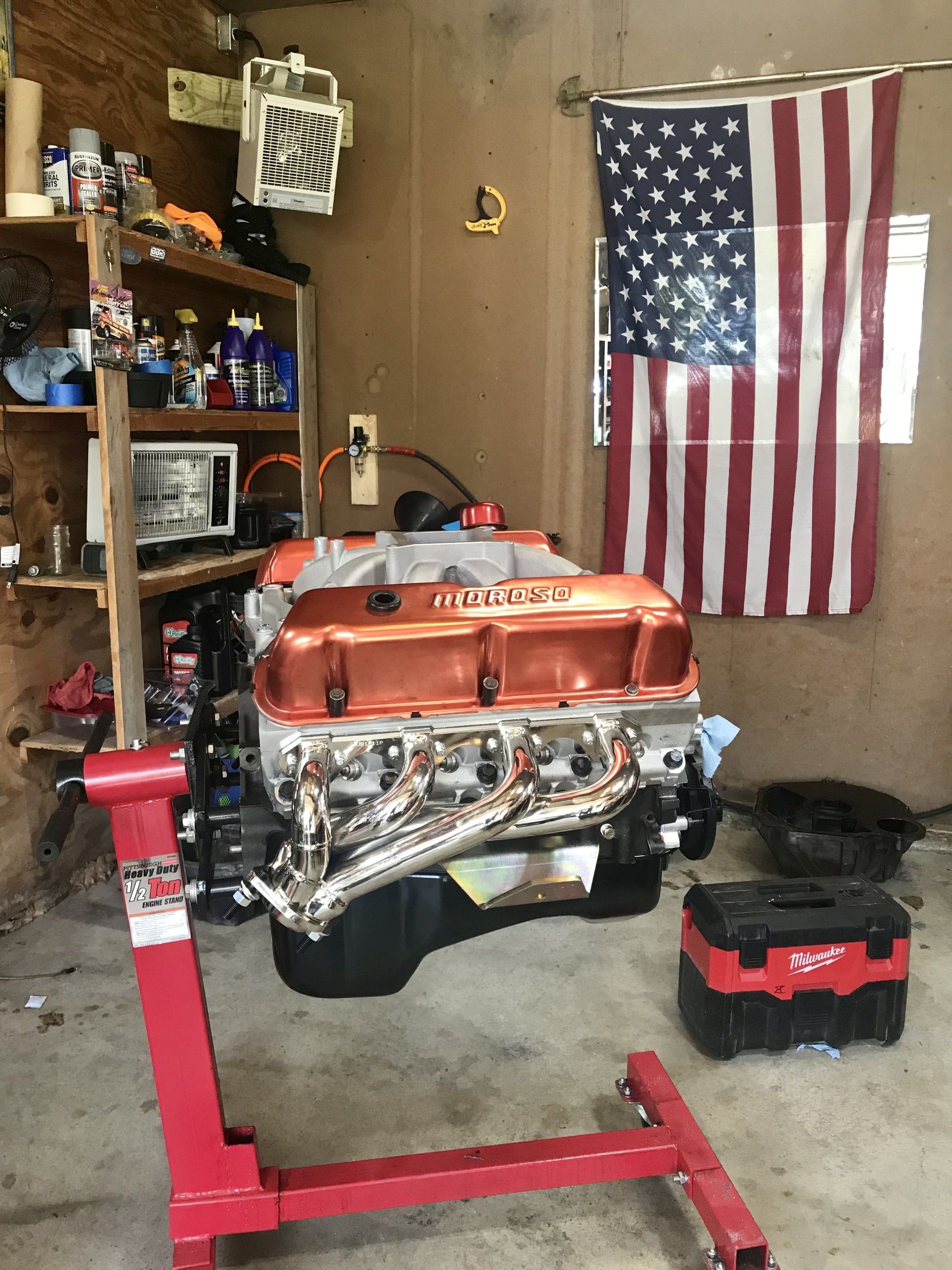 Engine on a red stand in a garage, with an American flag hanging on the wall.