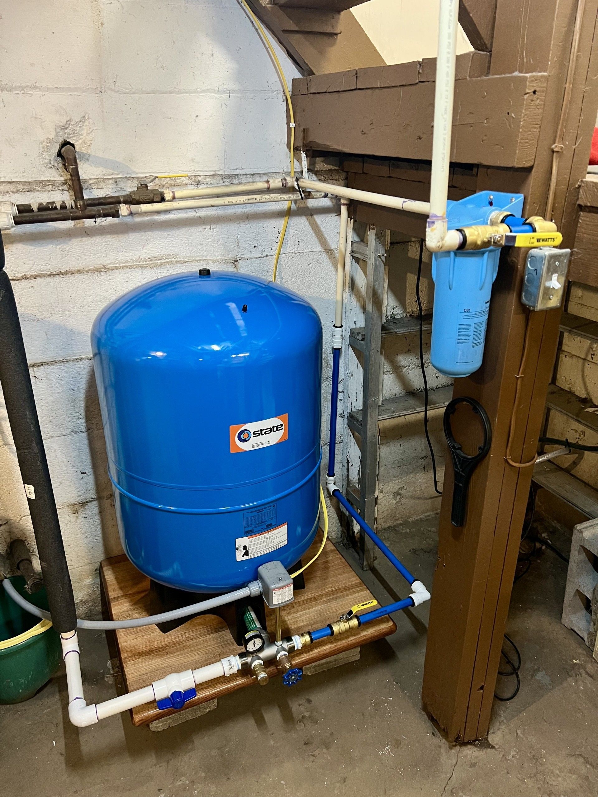 Blue water pressure tank with filter and pipes in a basement setting.