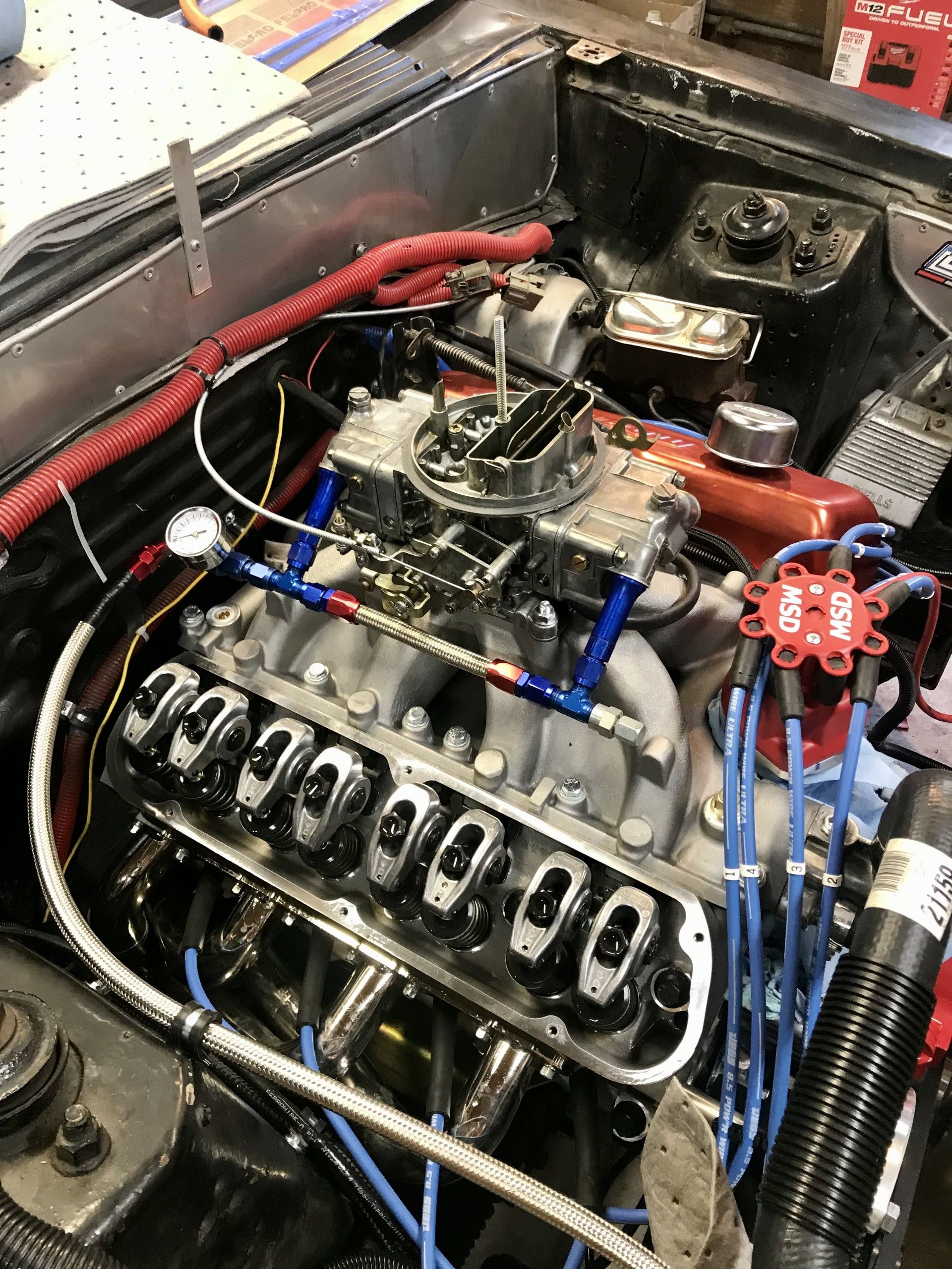 Engine bay with a V8 engine, fuel lines, and distributor, likely a classic car being restored.