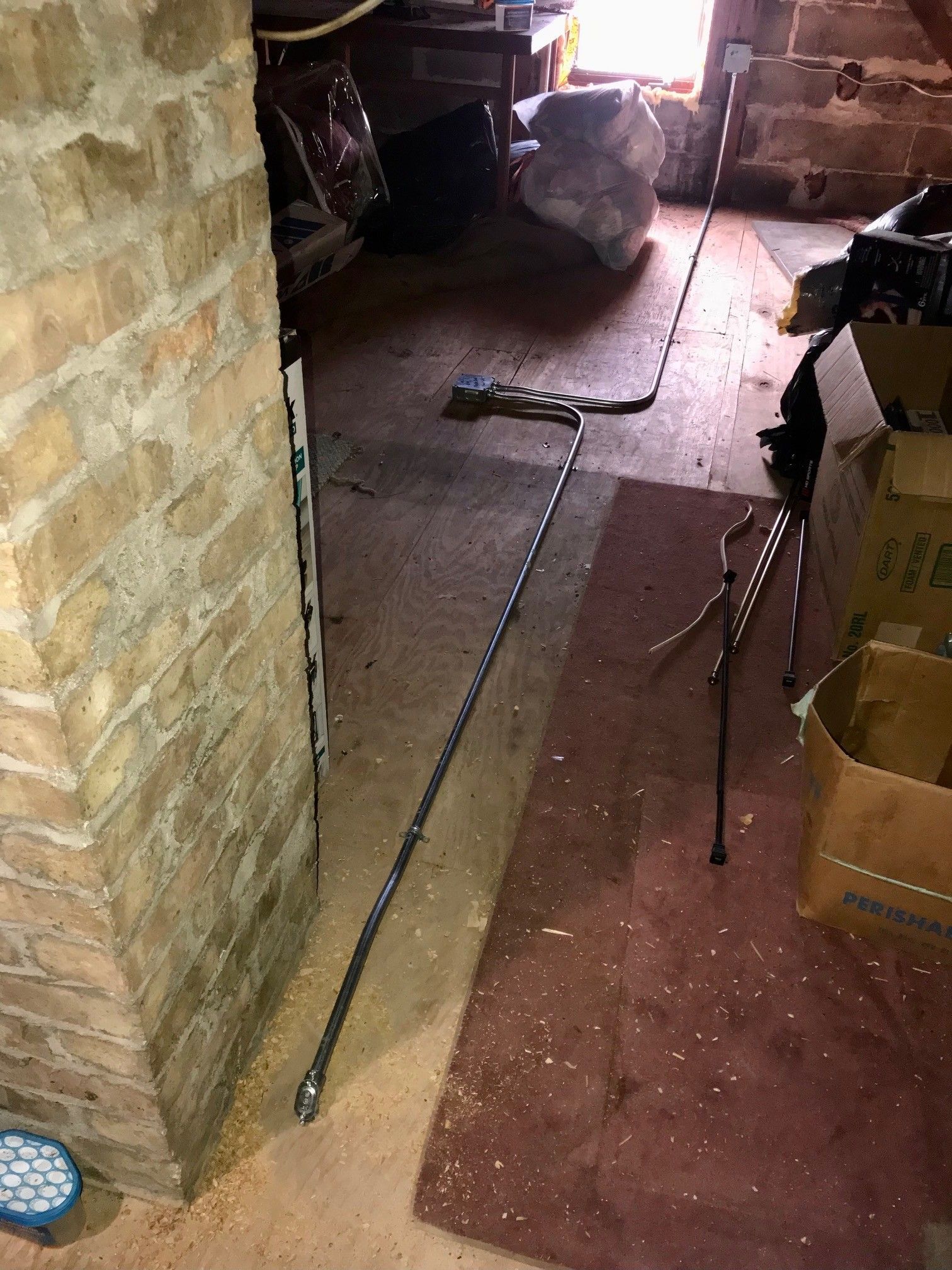 Basement with brick wall, long metal pipe, debris on floor.