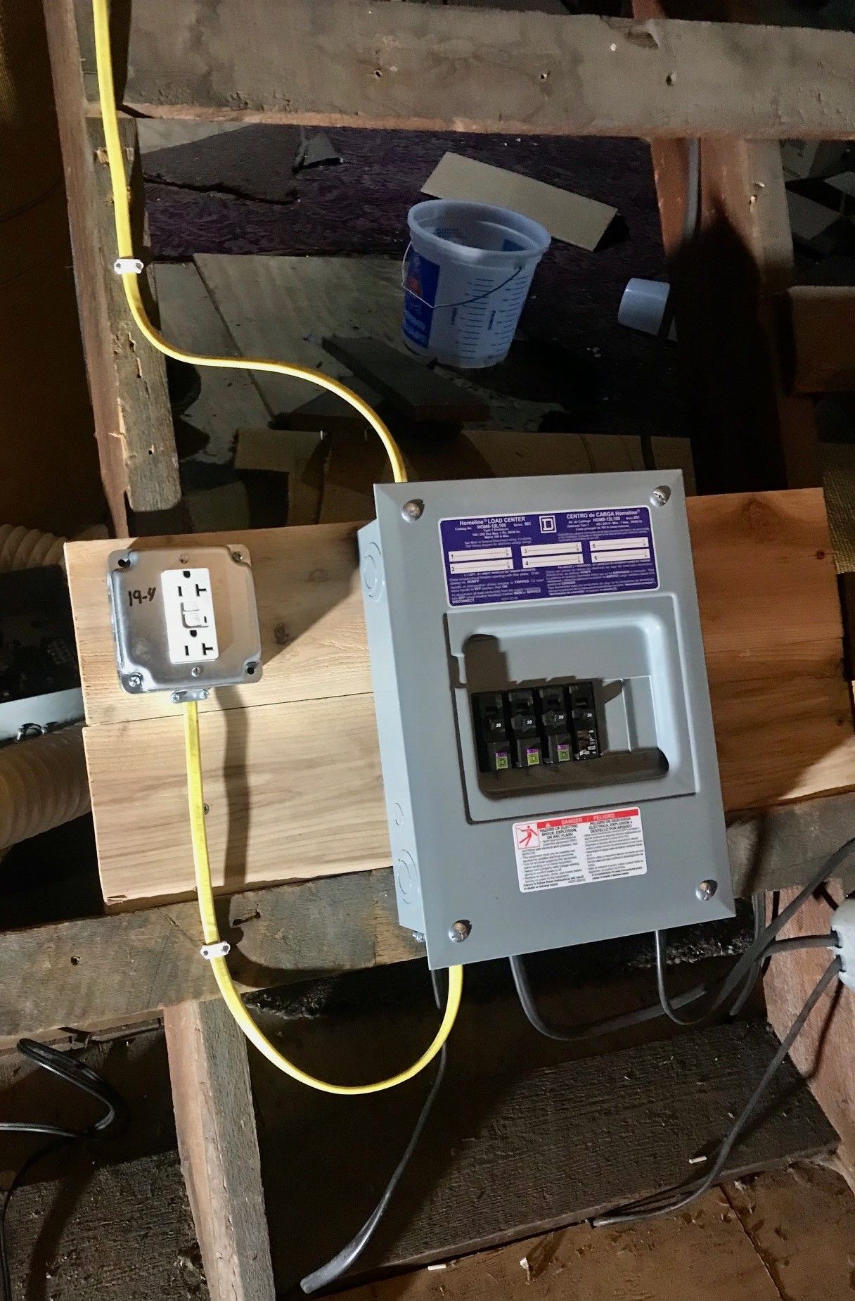 Electrical panel and switch mounted on wood. Yellow conduit runs between them.