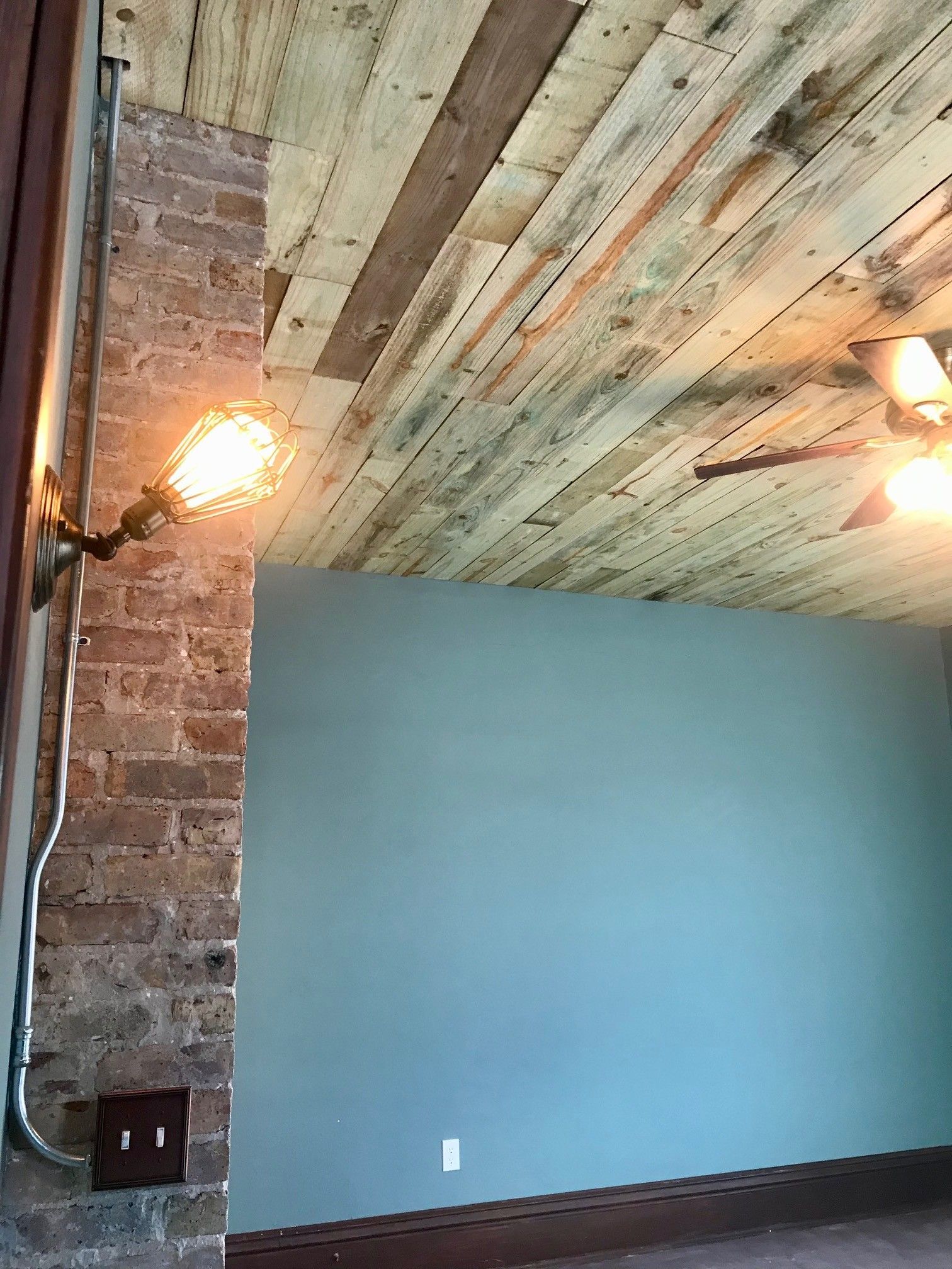 Industrial-style room with brick column, wooden ceiling, exposed bulb, and blue wall.